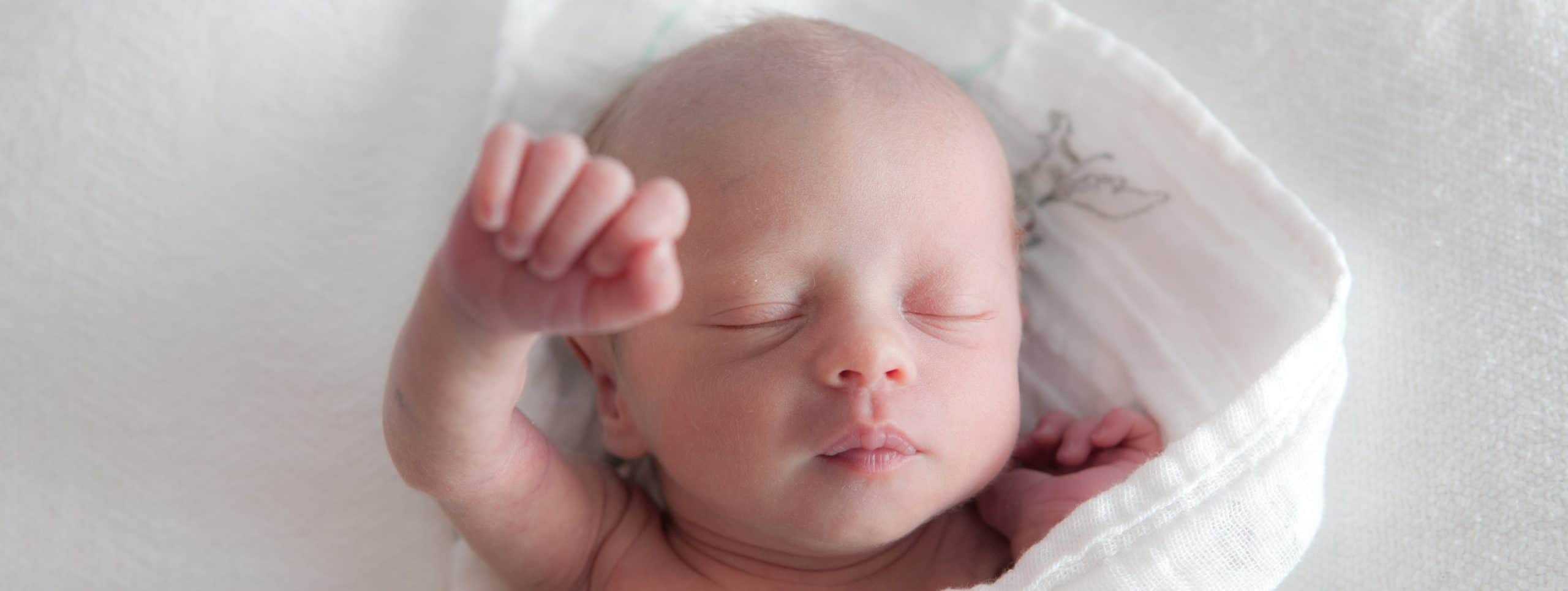 Main photo of baby with hand in the air.