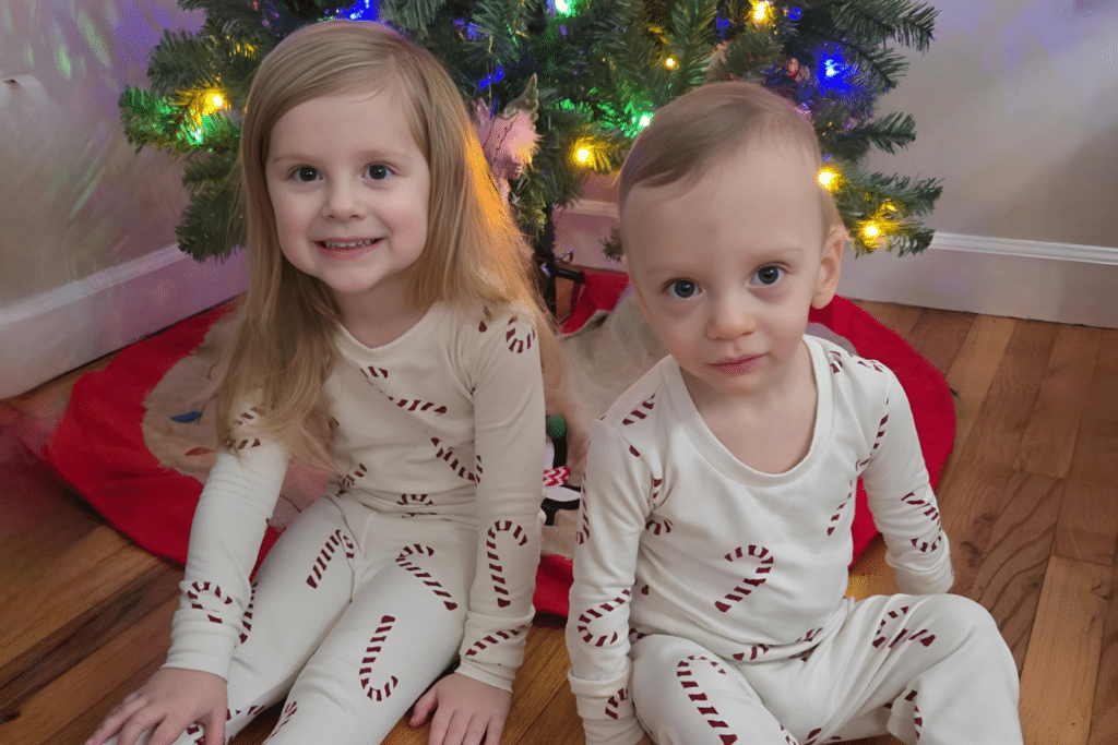 Young brother and sister wear matching pajamas in front of the Christmas tree